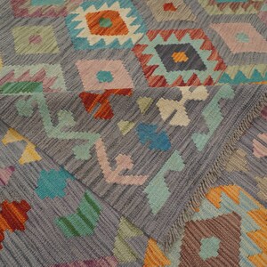 May include: A gray rug with a geometric pattern in shades of orange, red, blue, green, and pink. The rug has a fringe border.