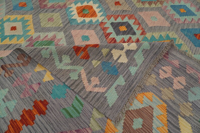 May include: A gray rug with a geometric pattern in shades of orange, red, blue, green, and pink. The rug has a fringe border.