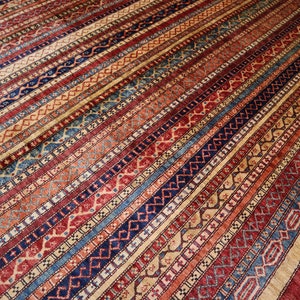 May include: A traditional rug with a colorful striped pattern featuring red, blue, and beige tones. The rug has a detailed geometric design with intricate details.