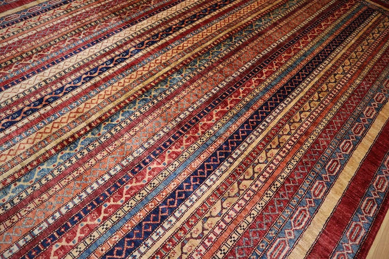 May include: A traditional rug with a colorful striped pattern featuring red, blue, and beige tones. The rug has a detailed geometric design with intricate details.
