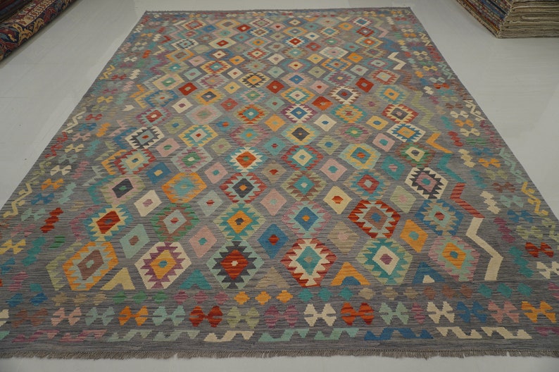 May include: A colorful rug with a geometric pattern in shades of red, blue, green, yellow, and orange. The rug has a gray background and a fringe border.
