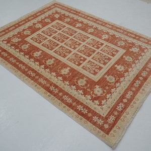 May include: A red and cream area rug with a floral pattern. The rug has a central square with a repeating pattern of stylized flowers and leaves. The border of the rug is a cream color with a repeating pattern of small flowers.