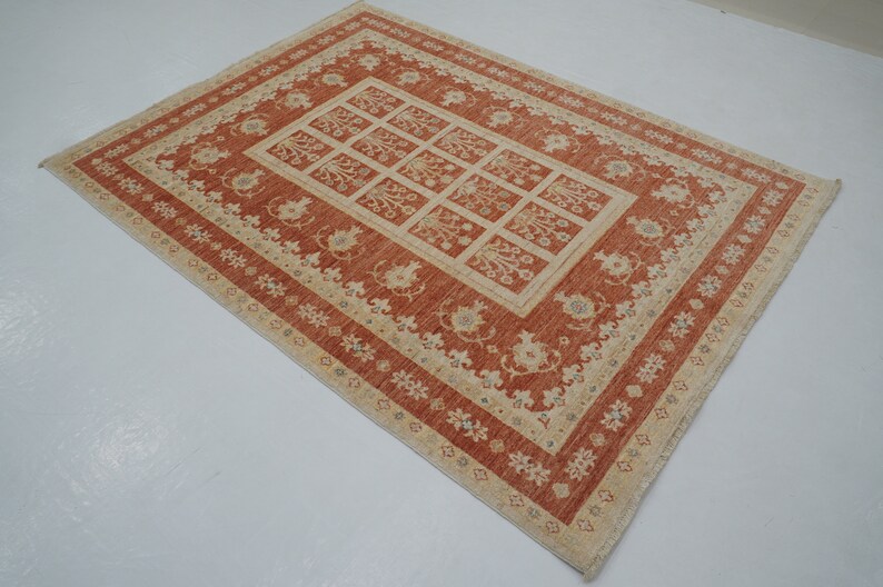 May include: A red and cream area rug with a floral pattern. The rug has a central square with a repeating pattern of stylized flowers and leaves. The border of the rug is a cream color with a repeating pattern of small flowers.