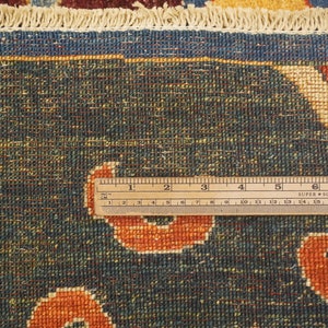 Op de afbeelding: Close-up van een blauw tapijt met een cr&egrave;mekleurige rand en een liniaal die 20 cm meet. Het tapijt heeft een herhalend patroon van oranje en cr&egrave;mekleurige vormen.