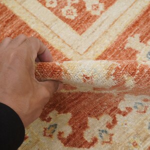 May include: Close-up of a hand holding a peach and cream colored rug with a floral pattern. The rug has a soft, fuzzy texture.