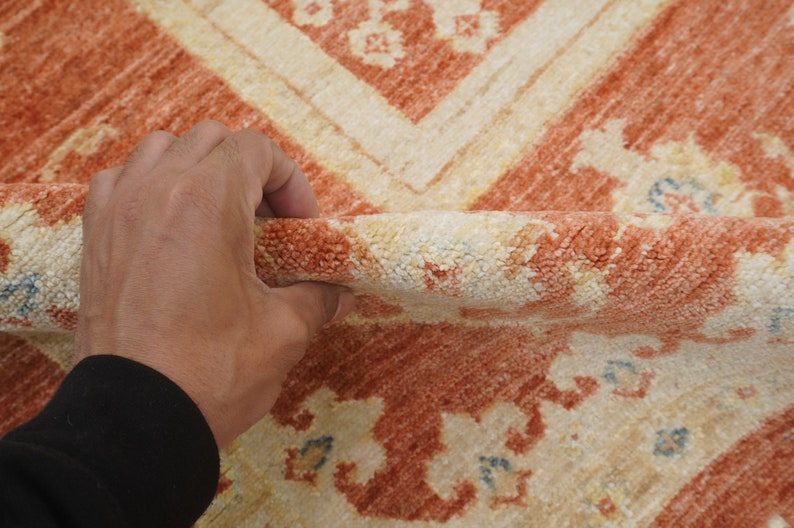 May include: Close-up of a hand holding a peach and cream colored rug with a floral pattern. The rug has a soft, fuzzy texture.