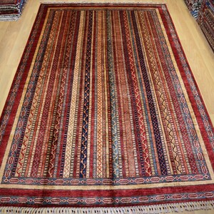 May include: A red, blue, and cream colored rug with a striped pattern and intricate border. The rug has a fringe on all sides.