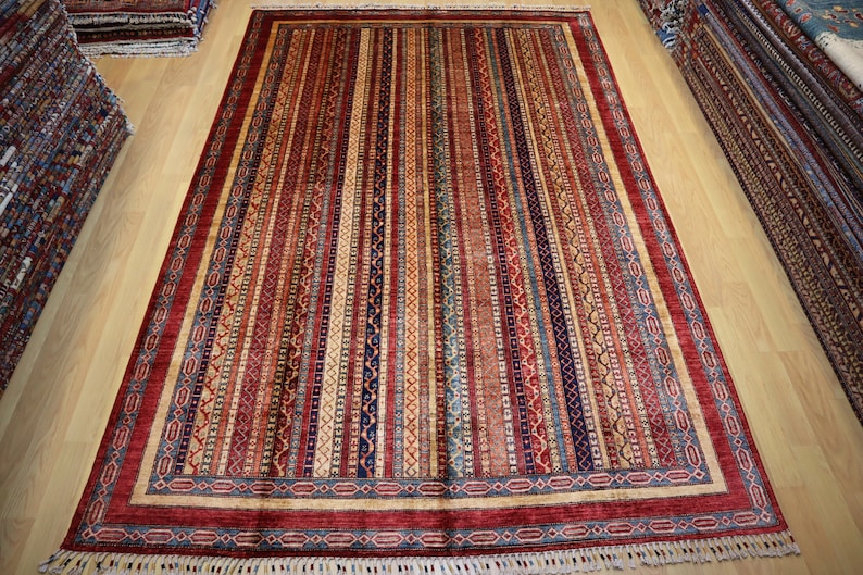 May include: A red, blue, and cream colored rug with a striped pattern and intricate border. The rug has a fringe on all sides.