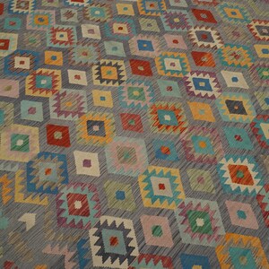 May include: A colorful rug with a geometric pattern in shades of blue, green, red, yellow, and orange. The rug has a gray background and a diamond-shaped pattern.