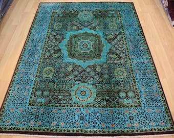 Può includere: Un tappeto blu turchese con un motivo geometrico verde scuro e marrone. Il tappeto ha un medaglione centrale con un disegno floreale.