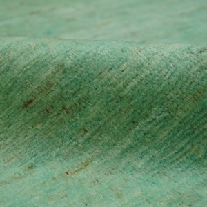 May include: Close-up of a soft, textured, teal-colored rug. The rug has a subtle pattern and a slightly uneven surface.