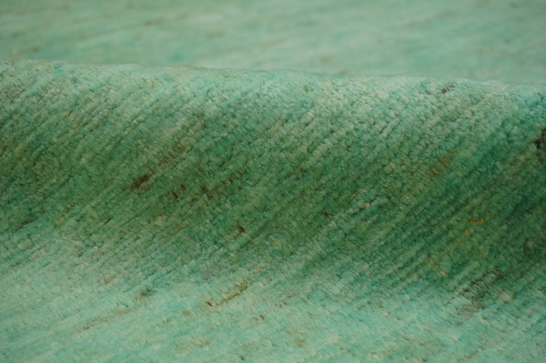 May include: Close-up of a soft, textured, teal-colored rug. The rug has a subtle pattern and a slightly uneven surface.