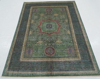 Può includere: Un tappeto rettangolare verde con un motivo intricato. Il tappeto presenta un disegno centrale con un medaglione rosso e blu, circondato da forme geometriche e motivi floreali. Il bordo è di una tonalità di verde più scura.