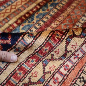 May include: A close-up of a colorful rug with intricate patterns in shades of red, blue, and cream. The rug is woven with a fine texture and has a traditional design.
