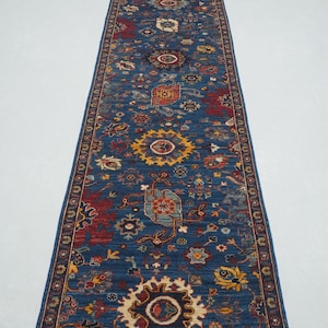 May include: A long blue runner rug with a traditional Persian design. The rug features intricate floral patterns, geometric shapes, and a central medallion in shades of red, yellow, and cream.