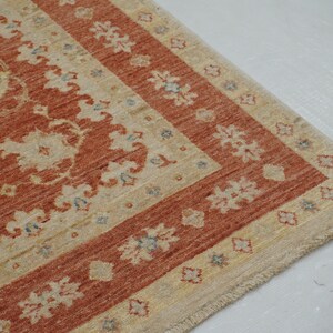 May include: A beige and rust-colored rug with a floral pattern and a fringed edge.