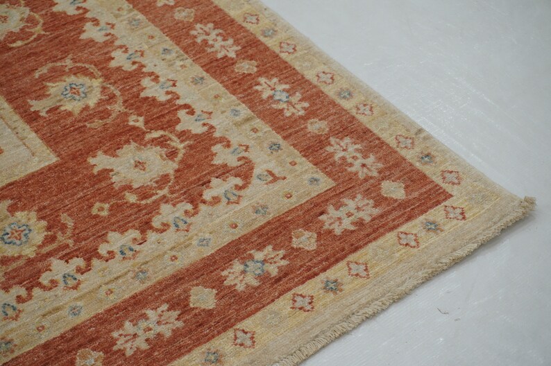 May include: A beige and rust-colored rug with a floral pattern and a fringed edge.