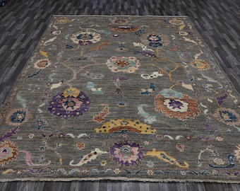 May include: A gray area rug with a floral pattern in shades of purple, blue, yellow, and orange. The rug has a fringed edge.