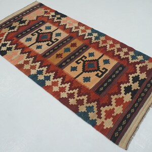 Puede incluir: Alfombra rectangular con un dise&ntilde;o geom&eacute;trico en tonos rojos, beige, azul y negro. La alfombra presenta un dise&ntilde;o central con formas de diamante y un borde con patrones repetidos. La alfombra est&aacute; probablemente hecha de material tejido.