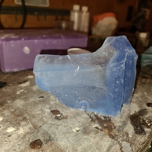 May include: A translucent blue resin casting with a rough, textured surface. The casting has a unique, abstract shape.
