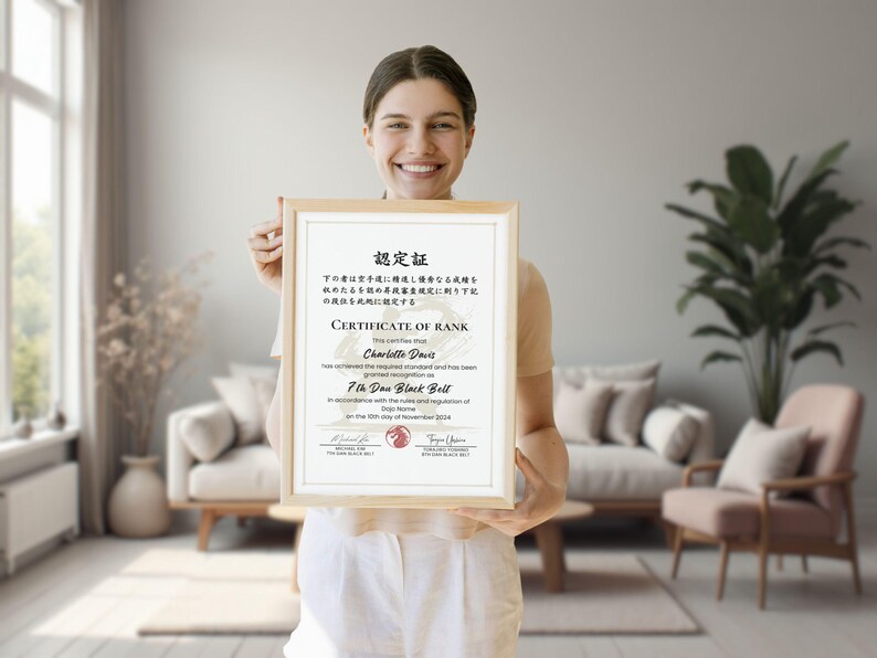 May include: A framed certificate with a light wood frame is held up. The certificate has text in English and Japanese. The text reads "Certificate of Rank" and "7th Dan Black Belt". The background shows a living room with a couch and plants.