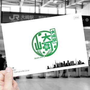 Op de afbeelding: Een witte kaart met een groen cirkellogo met Japanse karakters en de tekst "OSAKI Sta.". Het logo wordt omringd door een zwart silhouet van een stadsbeeld. De kaart bevat ook de tekst "JY24" en "Yamanote Line".