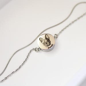 May include: A silver-toned metal bracelet featuring a circular charm engraved with a detailed illustration of a French Bulldog's face and the name Bandit written in a cursive script. The bracelet consists of a delicate chain and a snake chain.