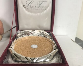 May include: A silver coaster set with a cork base, in a red velvet box. The box has the text "Silver Treasures by Godinger" on the lid.