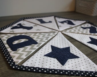 May include: A navy blue and white fabric banner with the letters "D.Y.L.A.N." and stars. The banner is made of different fabrics with polka dots, chevron, and solid white.