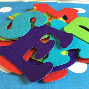 May include: A pile of felt letters in various colours, including red, green, blue, purple, and yellow. The letters are arranged in a random order and are all uppercase.