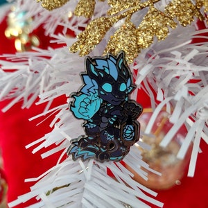 May include: A blue and black enamel pin featuring a cartoon dragon with blue flames. The dragon is holding a blue orb in its right hand and has a black and white striped tail.