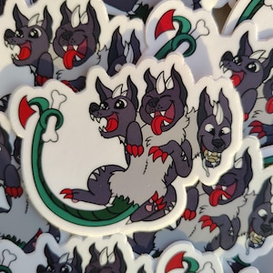 May include: A set of stickers featuring a cartoon two-headed dog with a green tail. The dog is smiling and has a tongue sticking out. The stickers are on a white background.