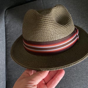 May include: A brown straw hat with a wide brim and a brown, white, and orange striped band.