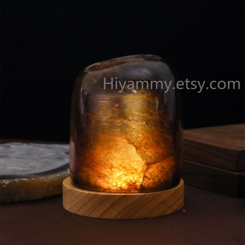 May include: A small, amber-colored, natural stone lamp with a warm, glowing light inside. The lamp is sitting on a wooden base. The text "Hiyammy.etsy.com" is visible in the image.