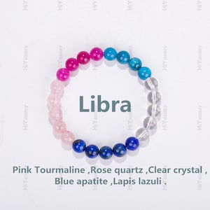 May include: A bracelet made of pink tourmaline, rose quartz, clear crystal, blue apatite, and lapis lazuli beads. The bracelet is arranged in a rainbow pattern and has the word "Libra" written in the center.