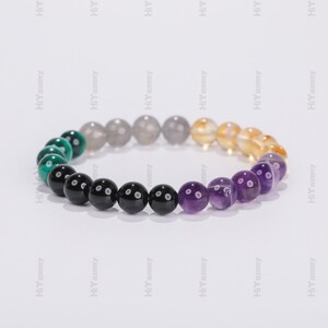 May include: A beaded bracelet with green, black, gray, yellow, and purple beads. The beads are arranged in a gradient pattern.