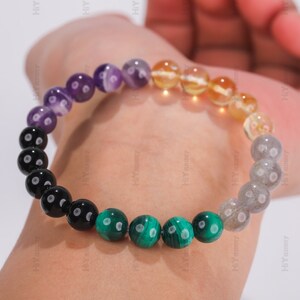 May include: A multi-colored beaded bracelet with black, green, yellow, purple, and gray beads. The bracelet is made of natural stones.