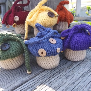 Puede incluir: Seis adornos de ganchillo con forma de hongo en varios colores, incluyendo verde, amarillo, rojo, azul y morado. Cada hongo tiene un botón en la parte superior y un tallo de ganchillo.