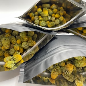 May include: Several silver pouches filled with dried, yellow-tipped, green seed heads. The seed heads have a spiky, cone-like appearance. The pouches are partially open, revealing the contents. The background is white.