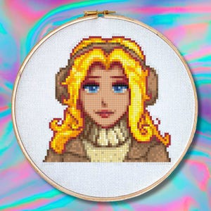 May include: Cross-stitch embroidery of a woman with blonde hair and blue eyes. The pixelated design features a brown coat and a cream-colored sweater. The embroidery is set in a wooden hoop against a colorful, swirling background.
