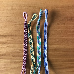 Peut inclure: Quatre bracelets d'amitié de différentes couleurs et motifs. Les bracelets sont faits de fil à broder coloré et ont un design simple de nœuds. Les bracelets sont attachés ensemble en haut et ont de longues extrémités lâches.