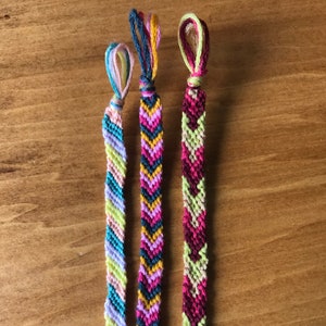 May include: Three friendship bracelets with chevron patterns in various colors, including pink, yellow, green, blue, and red.