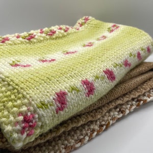 May include: A stack of knitted blankets, one with a green and white floral pattern and two in brown.