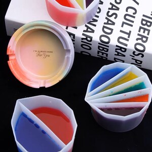 May include: Four silicone molds for resin crafts. The molds are shaped like a round ashtray and a round dish with multiple sections. The molds are filled with colorful resin, creating a rainbow effect.