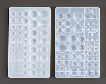 May include: Two clear silicone molds for making jewelry. The mold on the left has a variety of round and square shapes. The mold on the right has a variety of round, oval, heart, and square shapes.
