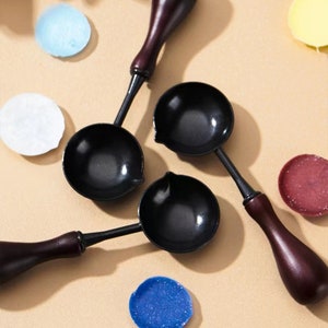 Könnte beinhalten: Drei schwarze Metall-Wachsstempel-Löffel mit Holzgriffen. Die Löffel haben eine abgerundete Schalenform und werden zum Schmelzen von Wachs zum Versiegeln von Briefumschlägen oder anderen Gegenständen verwendet.