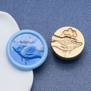 May include: A blue wax seal with a cloud and hands design, and a gold-colored brass stamp with the same design. The seal is round with a light blue border. The stamp is round with a wooden handle.