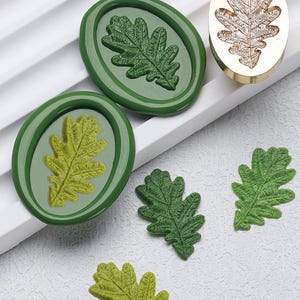 Pode incluir: Uma variedade de selos e carimbos de cera em forma de folha de carvalho verde e verde-amarelado. Os selos são ovais com um desenho de folha em relevo. Também está presente um carimbo de metal dourado com um desenho de folha de carvalho. Os itens estão dispostos em uma superfície branca.