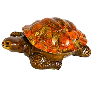 Può includere: Una statuetta di tartaruga in ceramica con un guscio marrone e accenti arancioni. La tartaruga è in posizione di camminata con la testa girata di lato.
