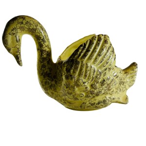 May include: A yellow ceramic swan planter with a gold floral pattern. The swan's neck is curved and its wings are spread out. The planter is designed to hold plants or flowers.